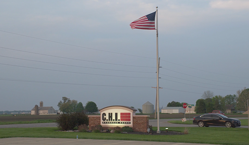 The lit street sign for C.H.I. Overhead Doors next to a flagpole with the American Flag waving in the wind. 